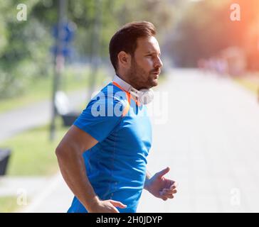 Zufriedener, gutaussehender Mann, der im Park läuft. Joggen am Morgen in der Stadt Stockfoto