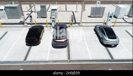 Luftaufnahme von drei Elektroautos, die ihre Batterien an einer elektrischen Ladestation auf einem Parkplatz laden Stockfoto