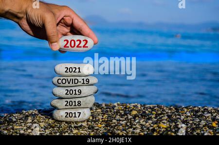 Frohes neues Jahr 2022 steht vor dem Konzept. Mann, der Stein zum Kiesturm hinzufügt, weil das neue Jahr 2022 das Jahr 2021 ersetzt. Schönes konzeptionelles Foto. Stockfoto