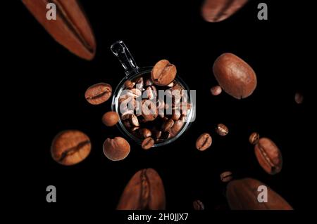 Kaffeebohnen fliegen in eine Tasse mit Kaffee isoliert auf schwarzem Hintergrund Draufsicht Stockfoto