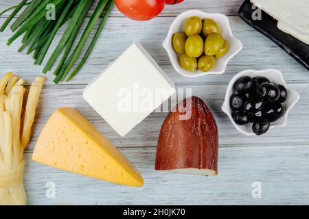 Draufsicht auf verschiedene Käsesorten mit grünen Zwiebeln und eingelegten Oliven auf grauem Holzhintergrund Stockfoto