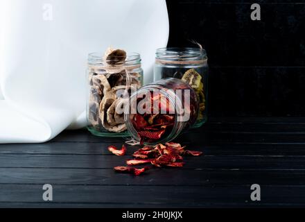 Seitenansicht von verschiedenen Trockenobstscheiben in Gläsern Erdbeerbanane und Kiwi auf schwarzem Hintergrund mit Kopierraum Stockfoto