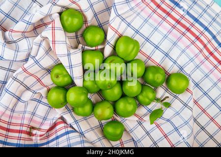 Draufsicht auf saure grüne Pflaumen, die auf karierten Stoffhintergrund verstreut sind Stockfoto