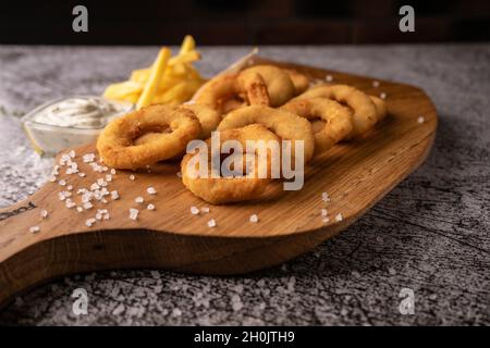 Selektiver Fokus. Gebratene Zwiebelringe in Semmelbröseln, in Öl gebraten. Mit natürlicher Sauce. Restaurant-Servieren. Auf dunklem Hintergrund. Für Menüs und Werbung Stockfoto