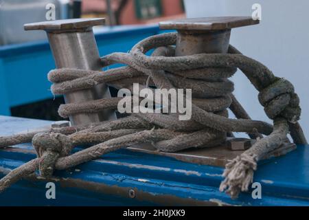 Schiffsbollard mit grauen Seilen, an dem ein blaues Boot festgemacht ist Stockfoto