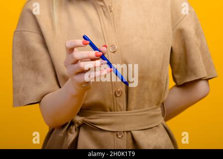Blauer Stift in Frauenhand isoliert auf gelbem Hintergrund. Stockfoto