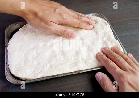 Hände, die den Teig in einer Pfanne zum Backen von Pizza oder Brot strecken Stockfoto