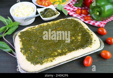 Hausgemachter Pizzateig mit Pesto-Sauce vor dem Backen in einer chaotischen Küche Stockfoto