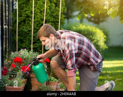 Mann mit Druckflasche und Bewässerung von Pflanzen in Blumentöpfen im Garten Stockfoto