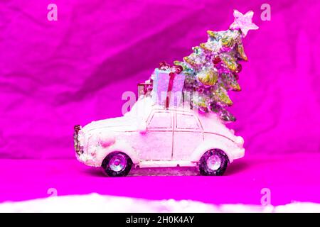 Spielzeugauto, Weihnachtsbaumgeschenke auf dem Dach auf einem rosa Hintergrund. Frohes Neues Jahr 2022. Stockfoto
