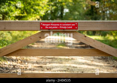 „Gefahr: Schusswaffen werden ständig verwendet. Don't Enter, Private Land', Zeichen auf einem hölzernen Tor auf dem Land. Stockfoto