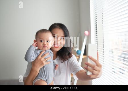 Die junge Mutter macht Selfie mit ihrem entzückenden kleinen Baby und lächelt Stockfoto