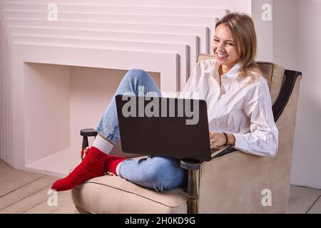 Lächelnde Frau, 24 Jahre alt, macht im Innenbereich Telearbeit mit einem Laptop. Stockfoto