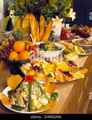 Hochformat, Buffetgerichte mit Spiegel, Blumen, Baguettes, französisches Brot, Kartoffelsalat, Geräucherter Lachs, Hühnergerichte auf einem hellen Holztisch Stockfoto
