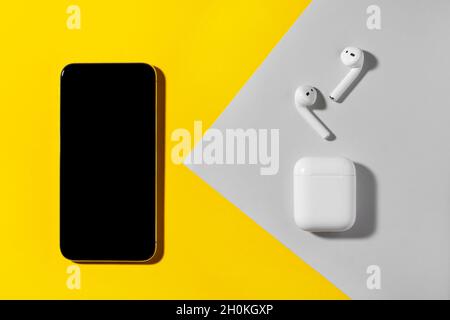 Smartphone und kabellose Kopfhörer auf gelbem und grauem Hintergrund. Stockfoto
