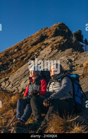 Mann und Frau in Sportkleidung sitzen auf dem Hügel. Schöne paar Reisende zu halten, genießen Hochland Landschaft, schönen Sonnenuntergang. Stockfoto