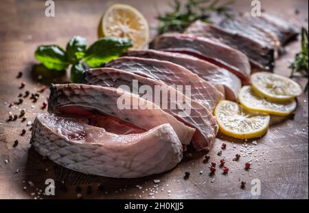 Portionierter Fischkarpfen mit Salz, Pfeffer, Zitrone und Kräutern auf dem Küchenbrett. Stockfoto