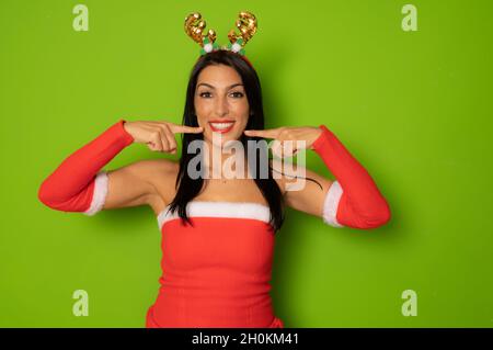 Schöne Frau im weihnachtsmann Kostüm zeigt Finger auf den Mund isoliert auf grünem Hintergrund. Stockfoto