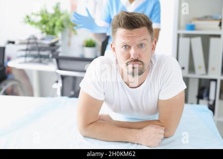 Junger trauriger Mann, der auf der Couch vor dem Proktologen in der Klinik liegt Stockfoto