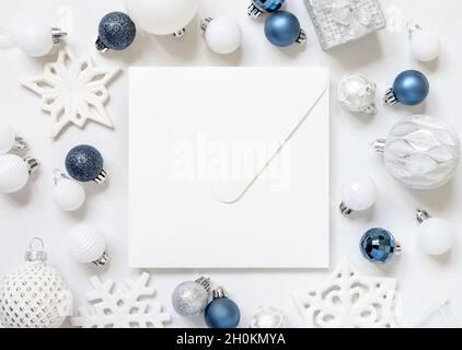 Leerer quadratischer Umschlag mit weißen, blauen und silbernen Weihnachtsdekorationen Draufsicht auf weißem Tisch. Winter Komposition mit Umschlag Mockup, Kopierraum Stockfoto