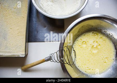 Geschlagene Eier in einer silbernen Schüssel, Mehl und Backform Stockfoto