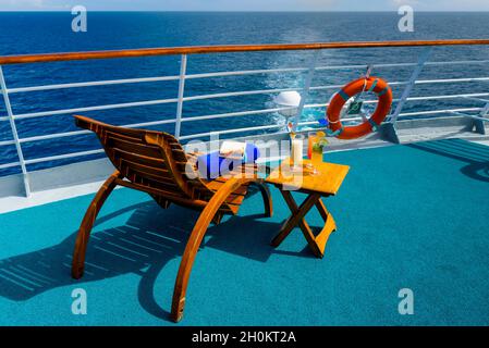 Sonnenliegen, um den Blick auf das Meer zu genießen, mit einem Cocktailtisch daneben auf dem Schiffsdeck. Stockfoto