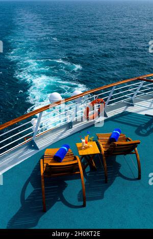 Sonnenliegen, um den Blick auf das Meer zu genießen, mit einem Cocktailtisch daneben auf dem Schiffsdeck. Stockfoto