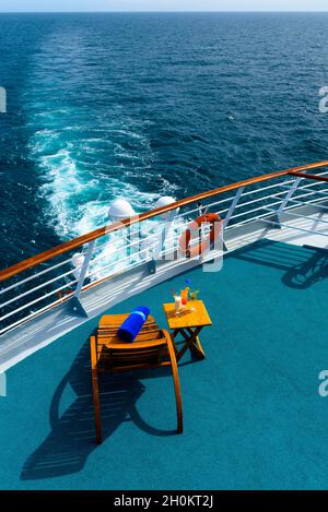 Sonnenliegen, um den Blick auf das Meer zu genießen, mit einem Cocktailtisch daneben auf dem Schiffsdeck. Stockfoto