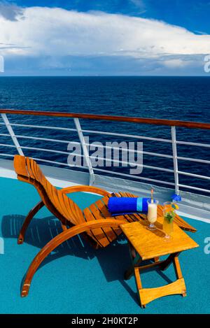 Sonnenliegen, um den Blick auf das Meer zu genießen, mit einem Cocktailtisch daneben auf dem Schiffsdeck. Stockfoto