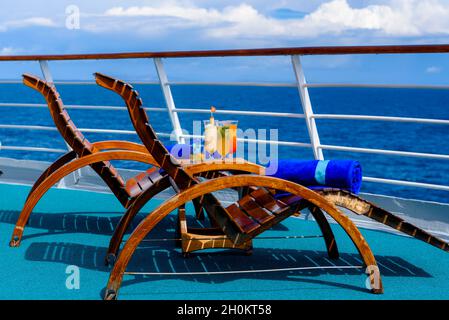 Sonnenliegen, um den Blick auf das Meer zu genießen, mit einem Cocktailtisch daneben auf dem Schiffsdeck. Stockfoto