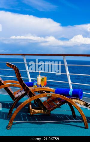 Sonnenliegen, um den Blick auf das Meer zu genießen, mit einem Cocktailtisch daneben auf dem Schiffsdeck. Stockfoto