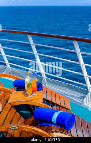 Sonnenliegen, um den Blick auf das Meer zu genießen, mit einem Cocktailtisch daneben auf dem Schiffsdeck. Stockfoto