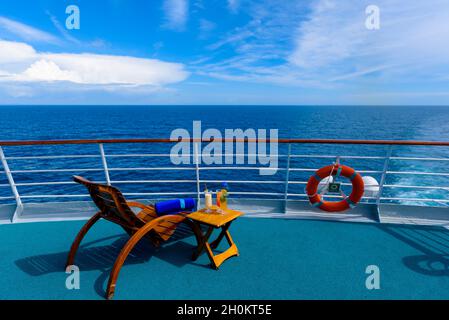 Sonnenliegen, um den Blick auf das Meer zu genießen, mit einem Cocktailtisch daneben auf dem Schiffsdeck. Stockfoto