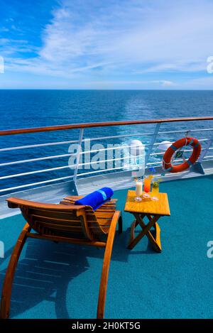 Sonnenliegen, um den Blick auf das Meer zu genießen, mit einem Cocktailtisch daneben auf dem Schiffsdeck. Stockfoto