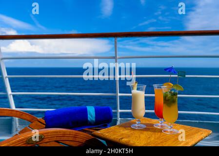 Sonnenliegen, um den Blick auf das Meer zu genießen, mit einem Cocktailtisch daneben auf dem Schiffsdeck. Stockfoto