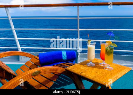 Sonnenliegen, um den Blick auf das Meer zu genießen, mit einem Cocktailtisch daneben auf dem Schiffsdeck. Stockfoto