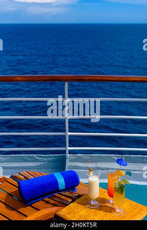 Sonnenliegen, um den Blick auf das Meer zu genießen, mit einem Cocktailtisch daneben auf dem Schiffsdeck. Stockfoto