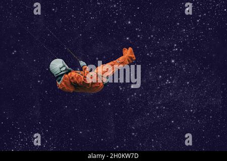 Astronaut mit orangefarbenem Raumanzug schwingt auf einer Seilschaukel im freien Raum Stockfoto