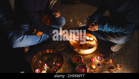 Mittelteil von zwei jungen indischen Männern, die sich auf die Diwali-Feier vorbereiten, während sie nachts draußen sitzen Stockfoto