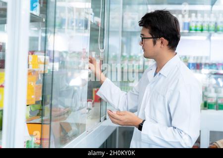 Ein männlicher Apotheker, der in der Apotheke eine Arzneibox und eine Kapselpackung hält. Stockfoto