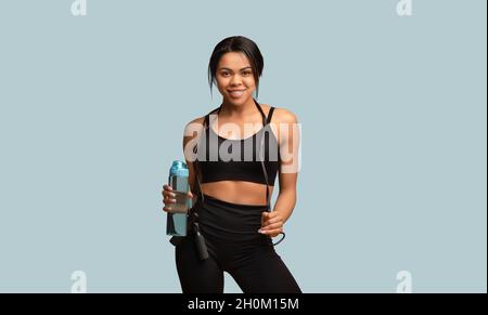 Fitnesstag. Fit afroamerikanische Frau in Sportbekleidung mit Springseil und Flasche Wasser, bereit für das Sporttraining Stockfoto