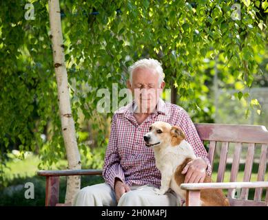 Alter Mann kuschelt Hund auf Bank im Garten im Frühjahr Stockfoto