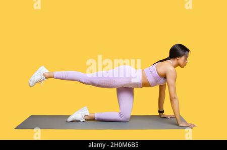 Körperformende Trainingseinheiten. Fit afroamerikanische Dame in Sportbekleidung tun Übung mit Bein heben, Training auf Yoga-Matte Stockfoto