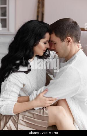 Schönes Paar in weißen, gemütlichen Pullovern, die während der Weihnachtszeit zu Hause posieren Stockfoto