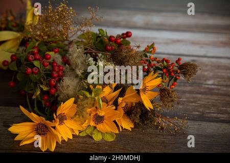 Herbststrauß aus gelben Blumen, Waldbeeren und trockenen Pflanzen auf einem Holztisch gesammelt Stockfoto