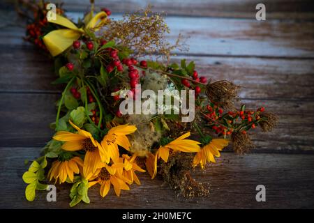 Herbststrauß aus gelben Blumen, Waldbeeren und trockenen Pflanzen auf einem Holztisch gesammelt Stockfoto