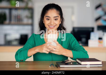Positive indische Frau, die mit Freunden plaudert und im Café arbeitet Stockfoto