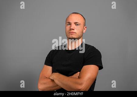 Lächelnder junger Mann, der mit geklappten Armen auf grauem Hintergrund steht Stockfoto