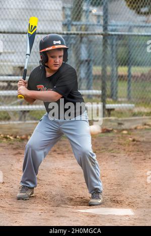 Junge Männer vor Teenagern, die sich auf den Ball konzentrieren, während sie Baseball in Uniform spielen Stockfoto