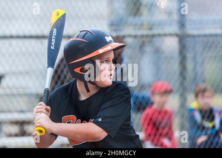 Junge Männer vor Teenagern, die sich auf den Ball konzentrieren, während sie Baseball in Uniform spielen Stockfoto